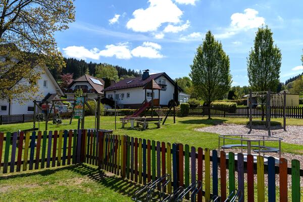 In dem eingezäunten Spielbereich gibt es für die Kinder ein Klettergerüst, eine Drehscheibe, Wippen, eine Schaukel und eine Rutsche. In der Mitte befindet sich eine Sitzgruppe mit Tisch.