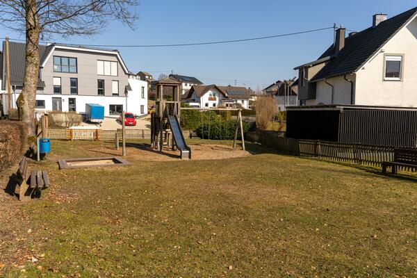 Der eingezäunte kleine Spielplatz liegt in einem Wohngebiet. Es gibt eine Schaukel mit Klettergerüst und einen Sandkasten.